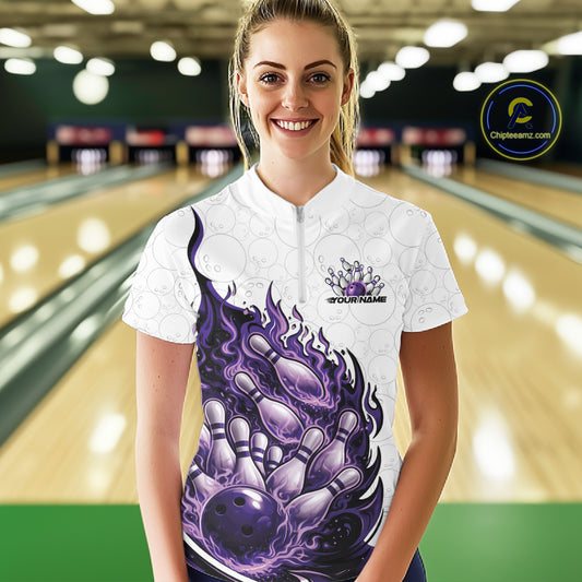 Front view female model at bowling lane wearing white, blue and purple quarter zip shirt showing flaming bowling ball striking pins with energetic cosmic fire illustration.