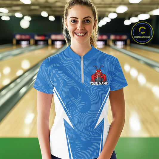 Front view of a happy female model in a bowling alley wearing a blue custom quarter-zip bowling shirt with a funny aggressive crawfish holding a bowling ball in a sportswear-style design.