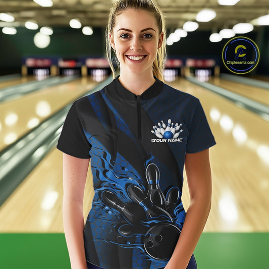 Female model in a bowling lane wearing a black and blue quarter zip shirt, front view showcasing fiery bowling ball knocking down pins with dynamic geometric artwork