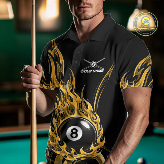 A man wearing a black polo shirt with a gold and yellow flame graphic and a 8-ball design, holding a pool cue in a dimly lit pool hall.