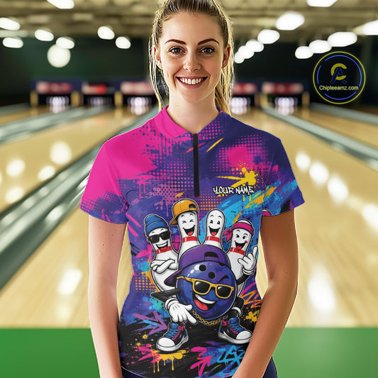 A woman stands in a bowling alley wearing a short-sleeve zip-front jersey with a colorful bowling-themed graphic print. The jersey features a pink and purple splatter design with cartoon bowling balls and pins, and the text 'YOUR NAME' on the chest.