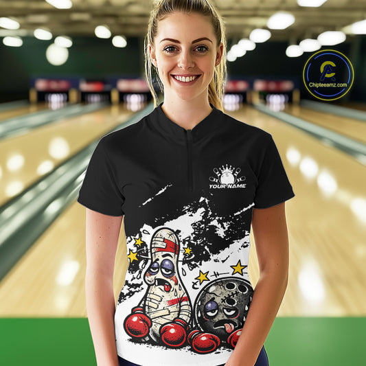 Female model in a bowling lane wearing a black and white quarter-zip shirt, cartoon boxing bowling ball and pin design with bold contrast.