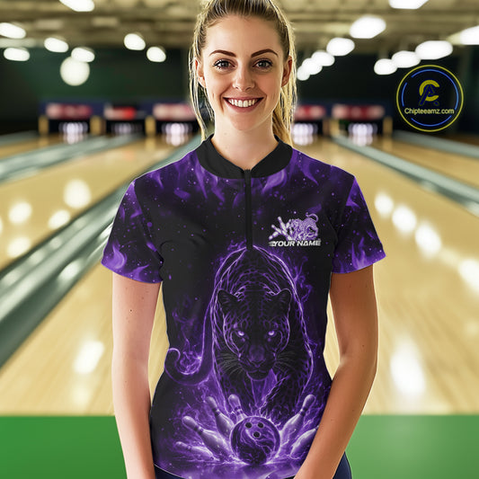 Front view of a female model in a bowling lane wearing a black quarter-zip shirt featuring a glowing electric panther in purple with bowling ball crashing through pins artwork.