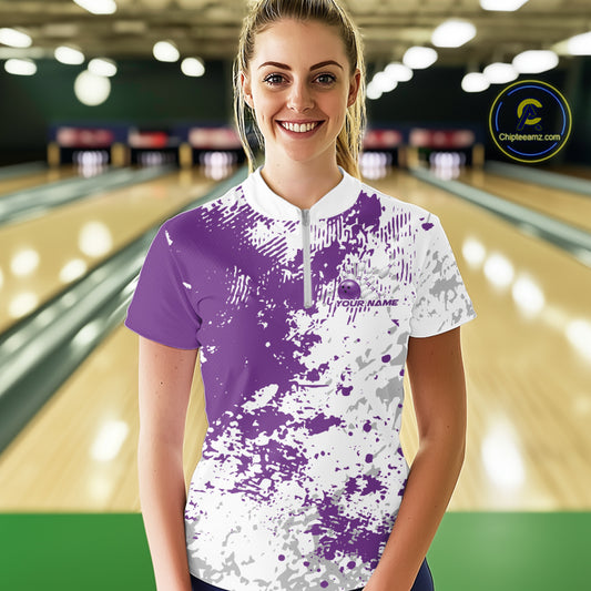 Front view of a female model in a bowling lane wearing a purple and white splatter bowling quarter-zip shirt with modern sporty graphics.