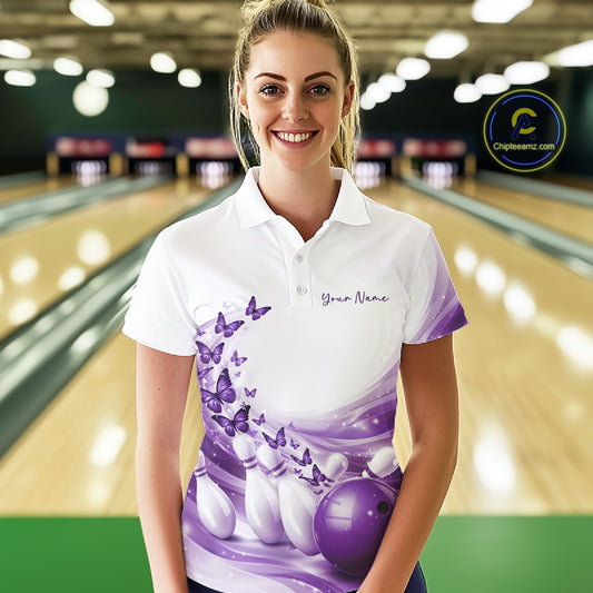Front view of a female model wearing a white and purple bowling polo shirt featuring butterfly accents and bowling graphics at the bowling lane.