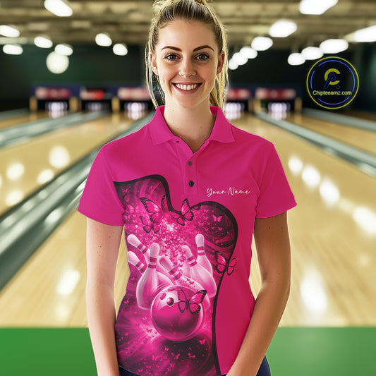 Female model wearing a pink bowling polo with butterfly artwork and bowling graphics, front view at the bowling lane