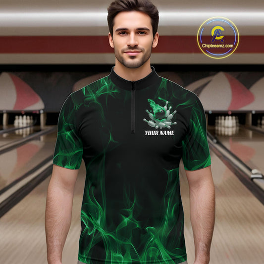 Male model at a bowling lane wearing a black and green bowling quarter-zip shirt with bowling strike artwork, scattered pins, and fiery accents.