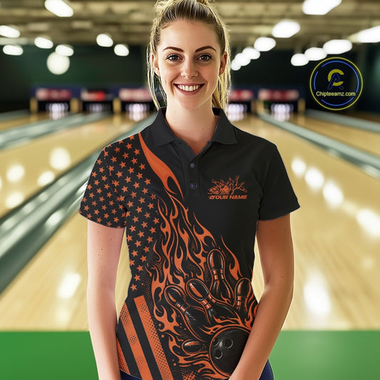 Female model at a bowling lane wearing a black bowling polo shirt with orange flame bowling strike artwork and patriotic graphics.