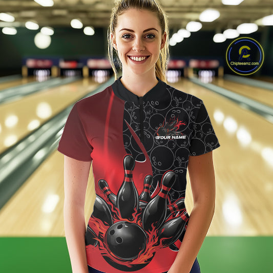 In a bowling lane, front view of a female model wearing a black and red bowling quarter-zip shirt, showcasing flaming bowling ball striking pins graphic with gradient pattern design.