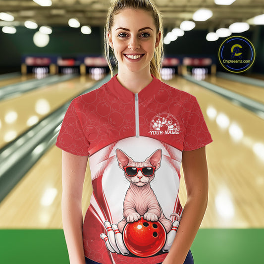 Female model at a bowling lane wearing a white and red quarter-zip bowling shirt with a sphynx cat in sunglasses resting against a bowling ball.