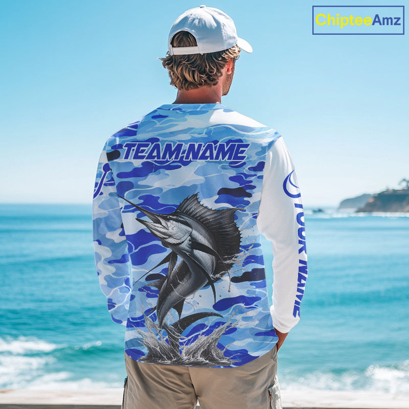 A man wearing a sailfish fishing shirt long sleeve with a large fish graphic and 'TEAM NAME' text, standing by the ocean.