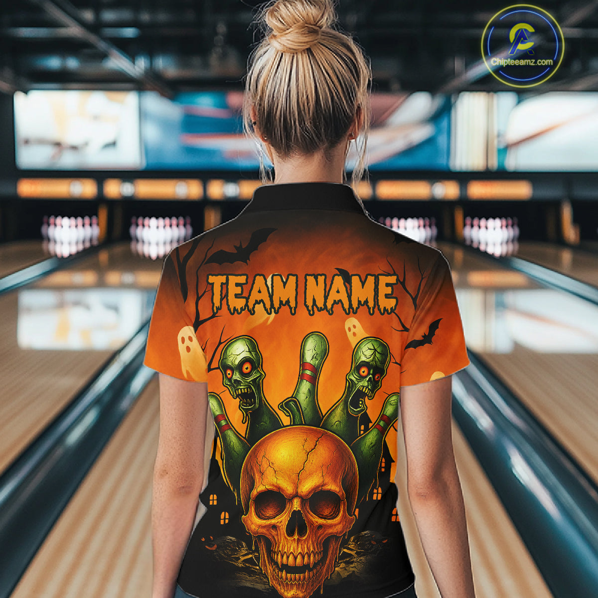 A woman viewed from behind wearing a short-sleeve bowling-themed shirt with a large Halloween graphic on the back, standing in a bowling alley. The shirt features a skull, green ghosts, bats, and the text 'TEAM NAME'.