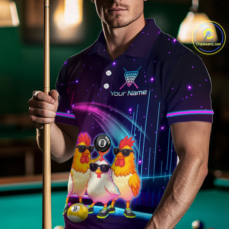 A man wearing a custom dark purple polo shirt with a cosmic starry pattern and cartoon chickens wearing sunglasses, holding a pool cue in a dimly lit pool hall. The shirt features a 'Your Name' placeholder logo