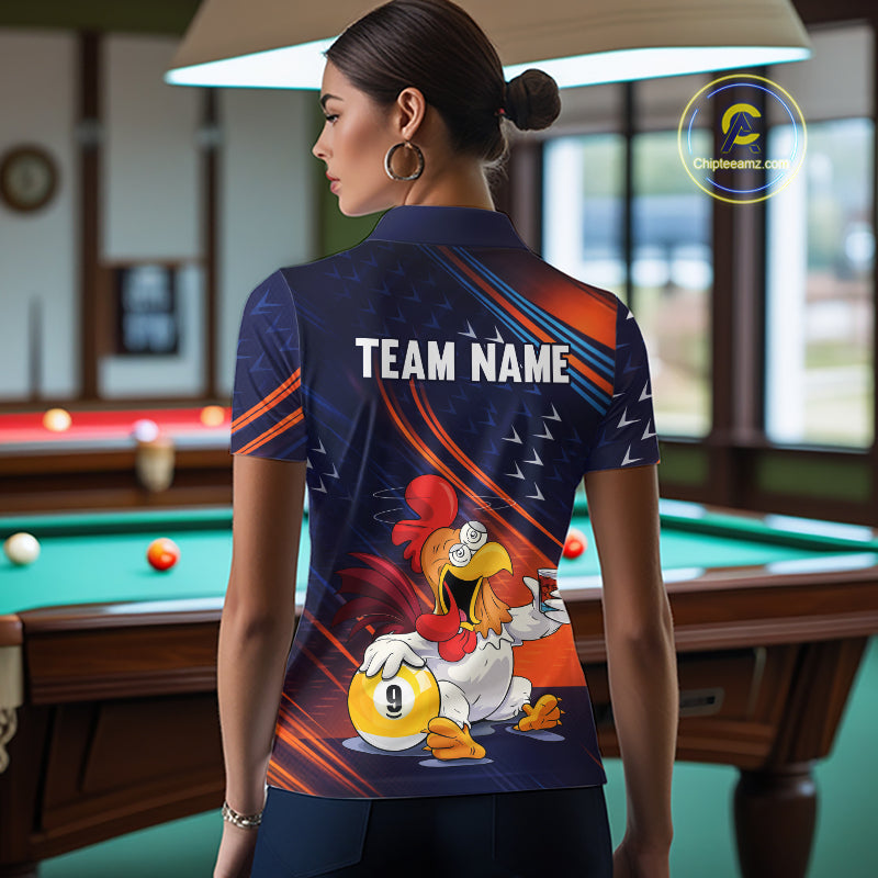 A woman stands in a billiards room wearing a custom-designed short-sleeve polo shirt. The shirt features a dark navy blue background with orange and white graphic stripes, the text 'TEAM NAME' printed across the upper back, and a cartoon rooster holding a billiard ball on the lower back.