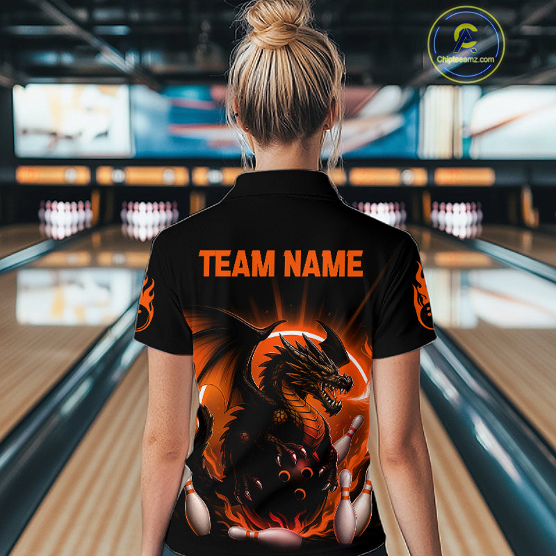 A woman viewed from behind wearing a black short-sleeve bowling shirt with a large fiery dragon graphic and orange 'TEAM NAME' text on the back, standing in a bowling alley.