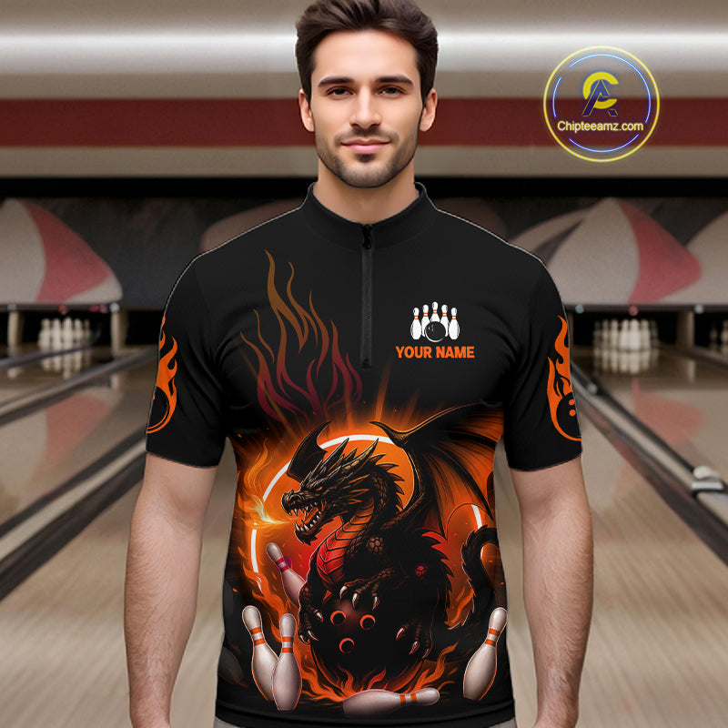 A man wearing a black short-sleeve zip-front shirt with a bold bowling-themed graphic print featuring a dragon, flames, bowling pins, and white text reading 'YOUR NAME'. The background shows blurred bowling lanes.