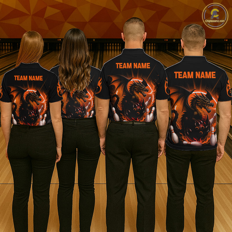 Four people standing in a bowling alley, viewed from behind, wearing matching black short-sleeve shirts with a large fiery dragon graphic and orange 'TEAM NAME' text on the back.