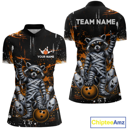 Front and back views of a women's short-sleeve polo shirt with a black base, orange paint splatter graphics, and a large raccoon mummified in bandages holding bowling balls. The front has a small bowling graphic with customizable text 'YOUR NAME' and 'TEAM NAME' on the back.