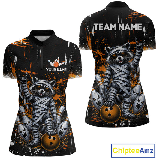 Front and back views of a women's short-sleeve polo shirt with a black base, orange paint splatter graphics, and a large raccoon mummified in bandages holding bowling balls. The front has a small bowling graphic with customizable text 'YOUR NAME' and 'TEAM NAME' on the back.