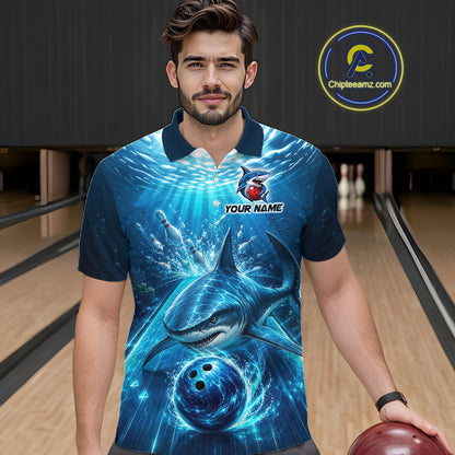 Man wearing a blue polo shirt with a shark and bowling ball design in a bowling alley.