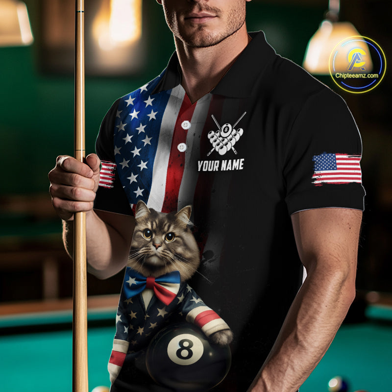 A front view of a custom black billiards polo shirt worn by a male model holding a pool cue. The shirt features a distressed US flag design on one side and a cartoon cat in vest with its paw on an 8-ball on the front. A 'YOUR NAME' text placeholder is positioned below a crossed pool cues icon. The background is a blurred billiards room with a green pool table.