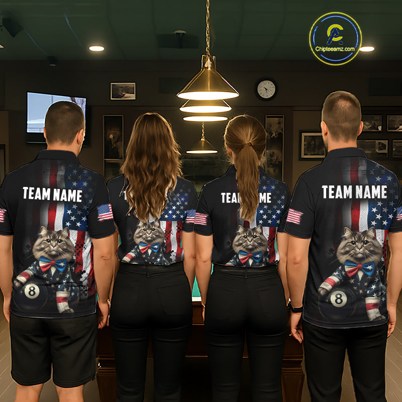 A back view of a team of four pool players standing in a line in front of a blue felt pool table in a billiards room. All four are wearing the back view of the custom black billiards polo shirt, which features a large distressed US flag pattern, a large white 'TEAM NAME' text placeholder, and a cat and 8-ball motif. 