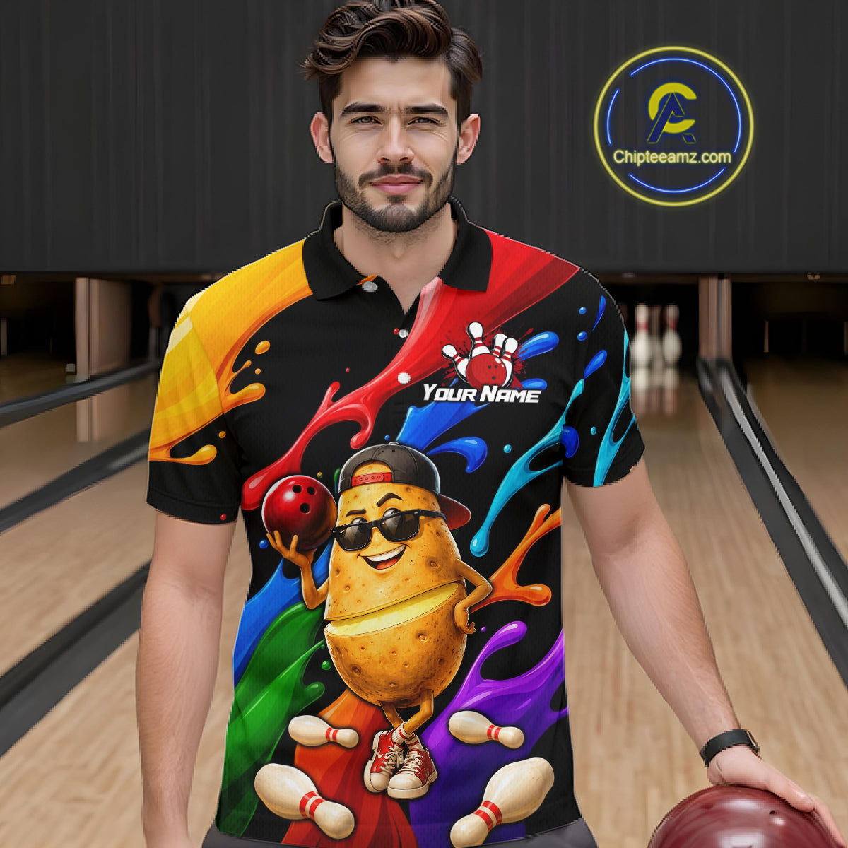 Man wearing a colorful shirt with a potato design holding a bowling ball in a bowling alley.