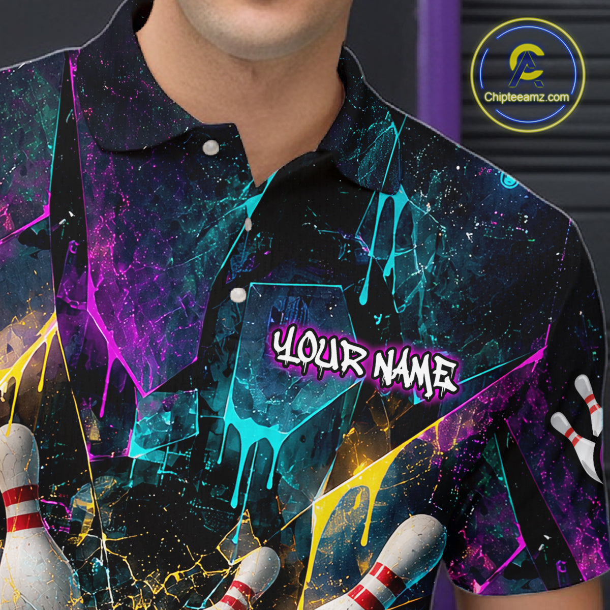 A close-up of a person wearing a short-sleeve polo shirt with a colorful bowling-themed graphic print. The shirt features a black base with neon paint-drip splashes in purple, blue, yellow, and pink, bowling pins at the bottom corners, and the text 'YOUR NAME' printed on the chest.