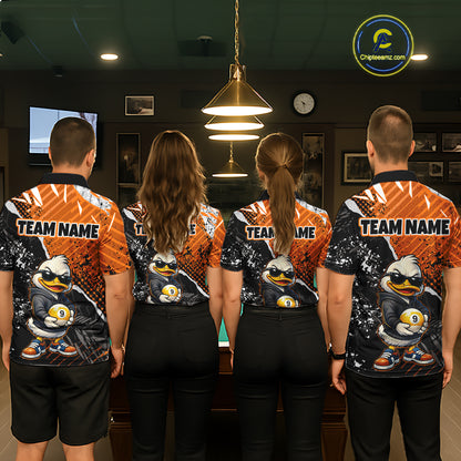Four people standing with their backs to the camera in a dimly lit indoor room, wearing matching custom-printed athletic jerseys. The jerseys feature a cartoon duck mascot in sunglasses holding ball 9, set against orange and black splatter patterns, with 'TEAM NAME' printed across the upper back.