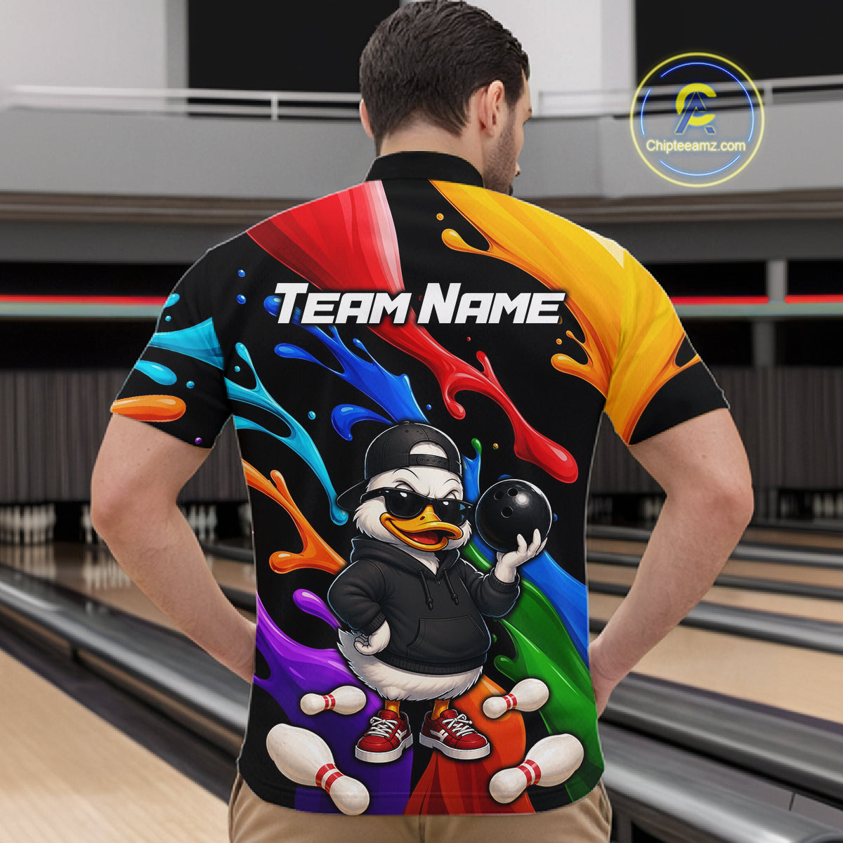 A man viewed from behind wearing a short-sleeve bowling shirt with a colorful graphic print. The shirt features a black base with vibrant paint splashes in red, yellow, blue, orange, green, and purple, a cartoon duck holding a bowling ball, and the text 'Team Name' across the upper back.