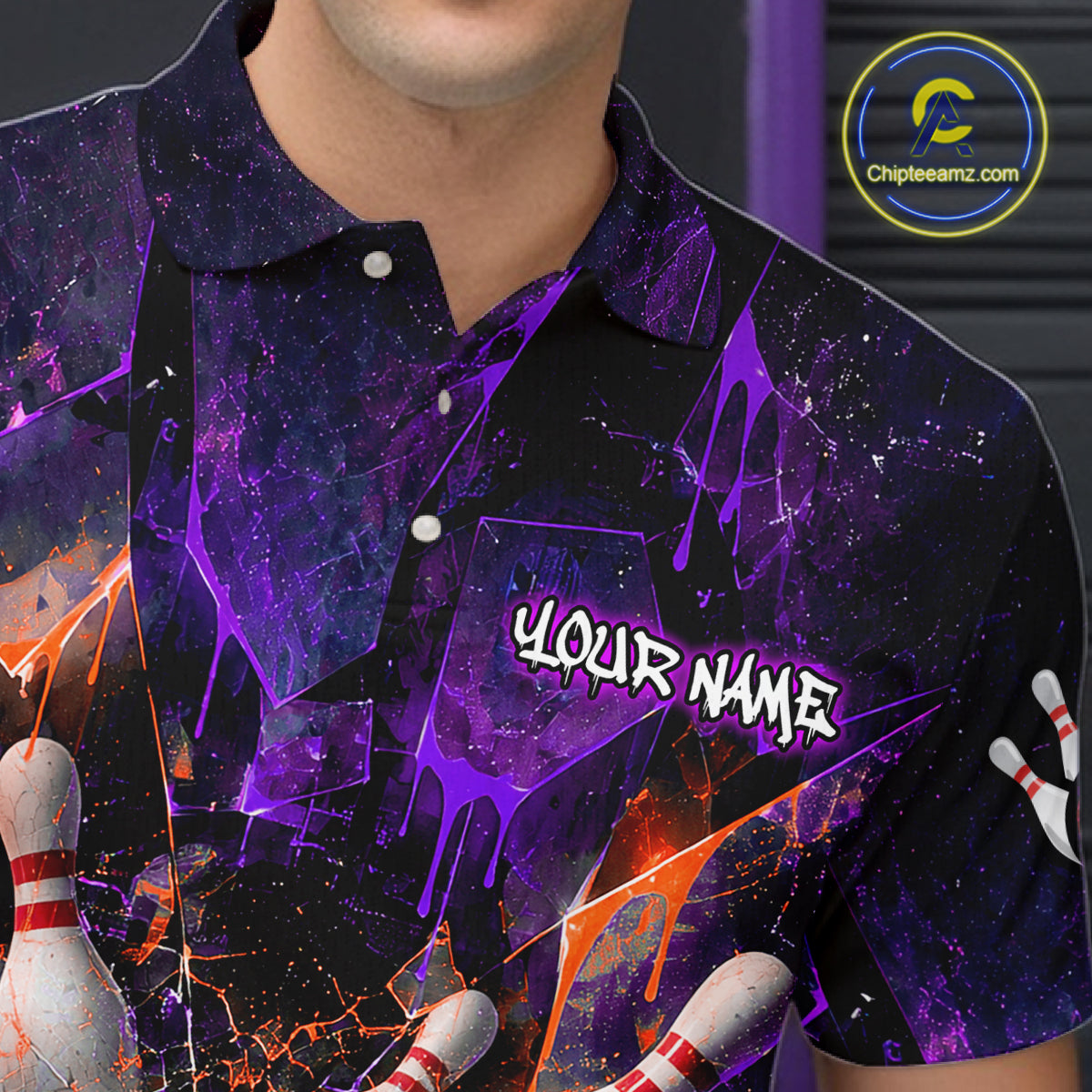 A close-up of a person wearing a short-sleeve polo shirt with a dark purple and black cosmic paint-splatter design, orange accents, bowling pins, and the text 'YOUR NAME' on the chest. 