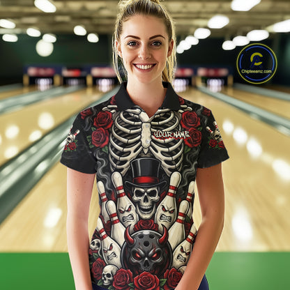A woman stands in a bowling alley wearing a black short-sleeve polo shirt with a detailed graphic print featuring a skeleton rib cage, bowling pins, skulls, roses, and a devil head. The shirt has 'YOUR NAME' printed on the chest.