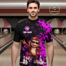 Load image into Gallery viewer, A man wearing a custom bowling-themed short-sleeve quarter-zip shirt with a black and bright purple splatter design, featuring a cartoon monkey graphic and the text 'YOUR NAME' on the chest. The background shows blurred bowling alley lanes.