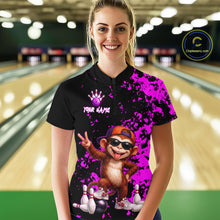 Load image into Gallery viewer, A woman standing in a bowling alley wearing a black short-sleeve bowling shirt with a bright purple paint splatter design, a cartoon monkey graphic, and a purple bowling pin crown logo. The background shows blurred bowling lanes.