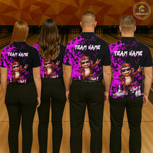Load image into Gallery viewer, Four people standing in a bowling alley, viewed from behind, wearing matching black short-sleeve shirts with a bright purple paint-splatter design, a cartoon monkey graphic, and the text 'TEAM NAME' across the upper back. 