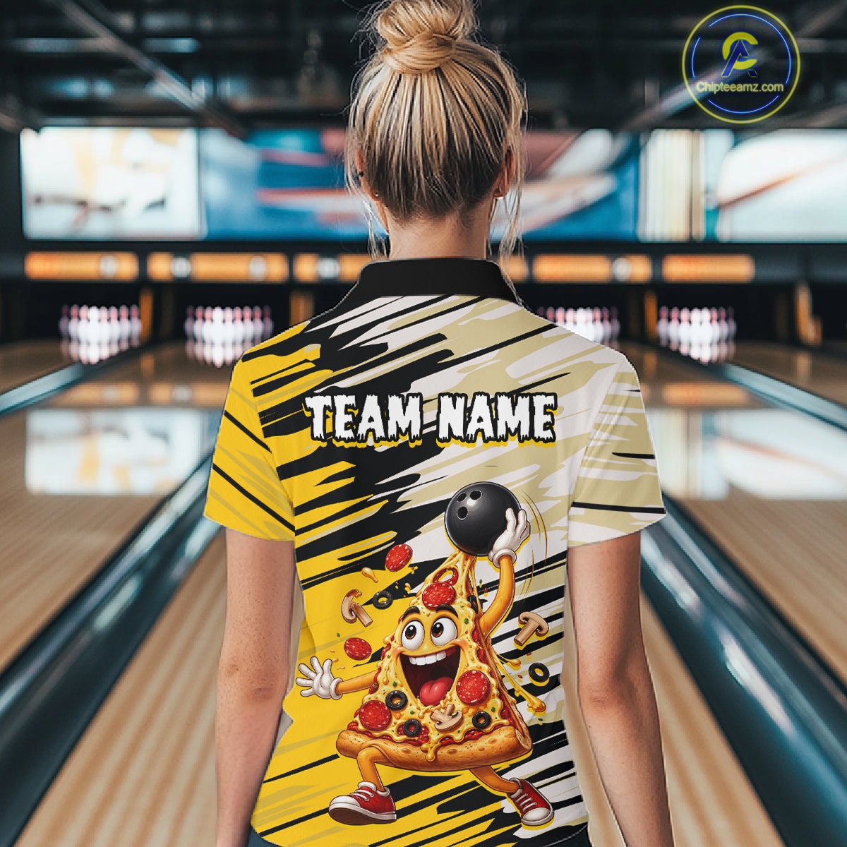 Person wearing a colorful bowling shirt with a pizza character design in a bowling alley.