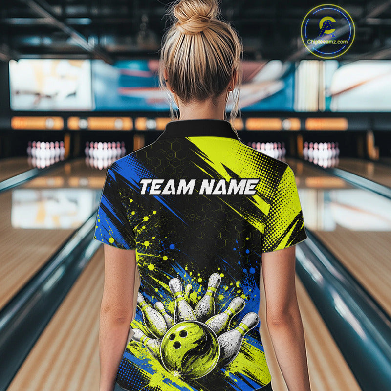 A woman viewed from behind in a bowling alley, wearing a short-sleeve collared shirt with a bold bowling-themed graphic print. The shirt features a black background with bright yellow and blue paint splatter effects, a bowling pin-and-ball design near the hem, and the text 'TEAM NAME' across the upper back.