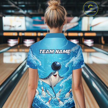 A woman viewed from behind wearing a blue short-sleeve bowling-themed shirt with a cartoon stingray catching a bowling ball and pins, set in a bowling alley. The shirt has 'TEAM NAME' printed on the back.