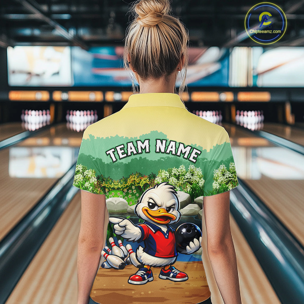 Person wearing a bowling-themed shirt with a cartoon duck character in a bowling alley.