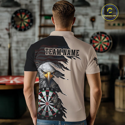 Person wearing a beige and black darts polo featuring a bald eagle, torn-flag graphics, dartboard designs, and custom team text.