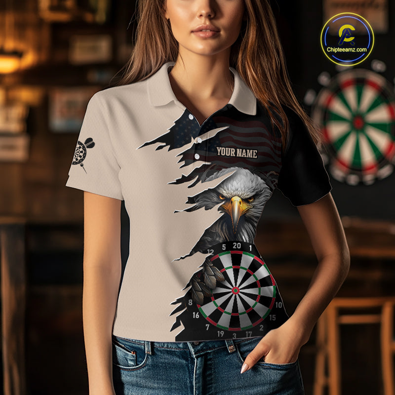 Person wearing a beige and black darts polo featuring a bald eagle, torn-flag graphics, dartboard designs, and custom team text.