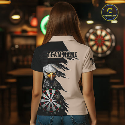 Person wearing a beige and black darts polo featuring a bald eagle, torn-flag graphics, dartboard designs, and custom team text.