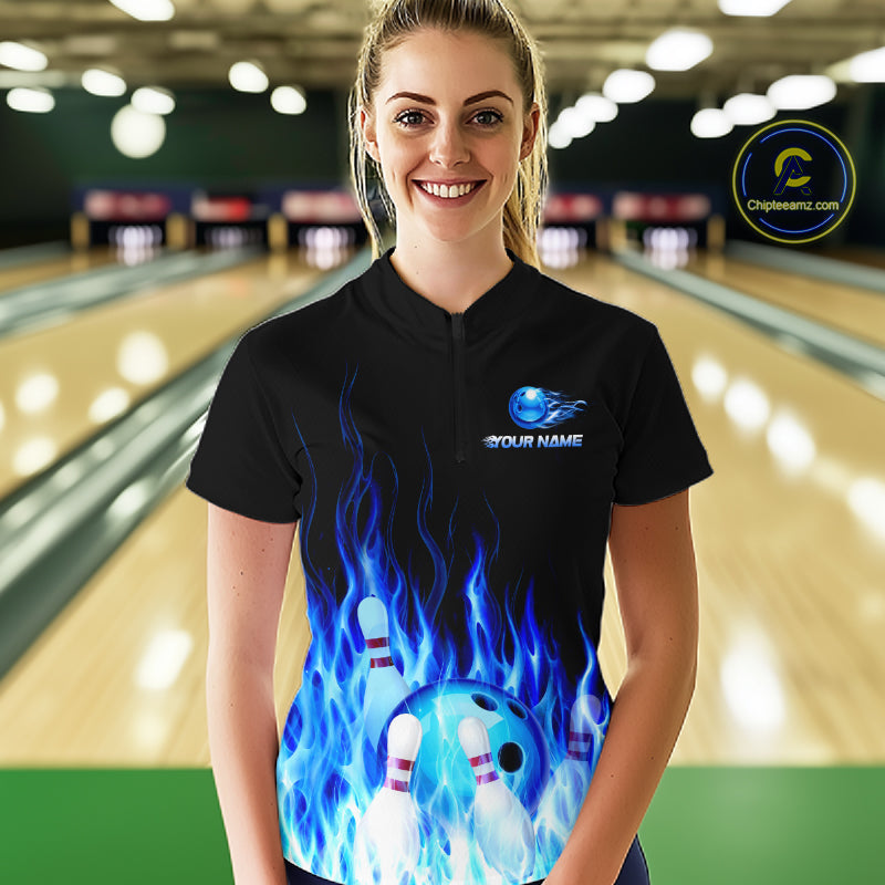 Person wearing a black bowling shirt with blue flame design and logo in a bowling alley.