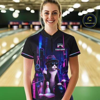 A woman stands in a bowling alley wearing a black short-sleeve polo shirt with a colorful neon cat graphic on the front. The shirt features a cat wearing a hat and sunglasses with bowling pins and a bowling ball, plus the text 'YOUR NAME' and 'Chipteeamz' on the chest and as a logo watermark.