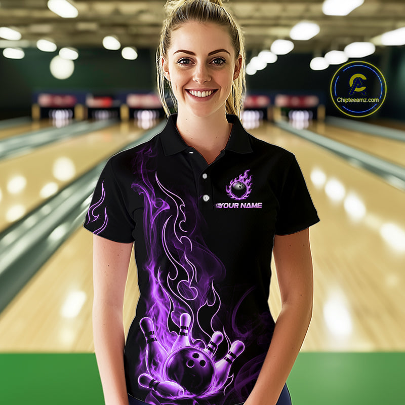 A woman stands in a bowling alley wearing a black short-sleeve polo shirt with a purple flame graphic and bowling pin/ball design on the front. The shirt has a custom placeholder logo and text.