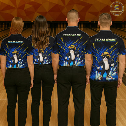 Four people standing with their backs to the camera in a bowling alley, wearing matching dark navy short-sleeve shirts with a colorful penguin graphic and 'TEAM NAME' text on the back, paired with black pants.