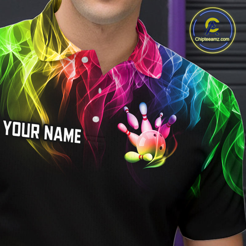 A close-up of a person wearing a black short-sleeve polo shirt with a vibrant rainbow smoke graphic and a bowling pin hand graphic on the chest. The shirt also features the text 'YOUR NAME' on the left chest and a circular 'Chipteeamz.
