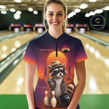 A woman wearing a custom short-sleeve bowling-themed polo shirt with a raccoon graphic and 'YOUR NAME' text, standing in a bowling alley. 