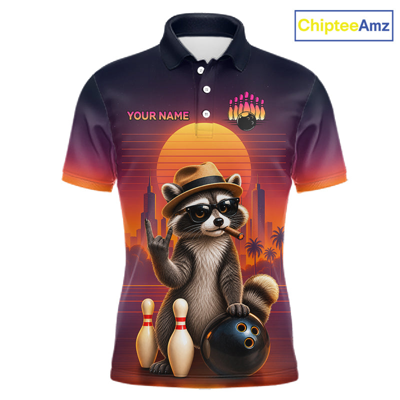 A short-sleeve polo shirt with a dark navy-to-orange gradient background and a large retro-style raccoon graphic on the front. The raccoon wears a hat and sunglasses and poses with bowling pins, bowling balls, and bowling pins against a sunset cityscape.