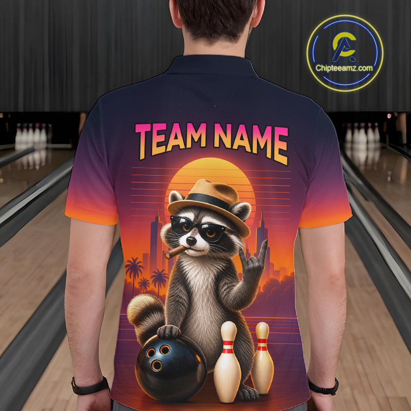 A person standing in a bowling alley wearing a short-sleeve collared shirt from the back. The shirt features a colorful retro-style graphic of a raccoon wearing a hat and sunglasses, holding a bowling ball beside bowling pins, with the text 'TEAM NAME' above.